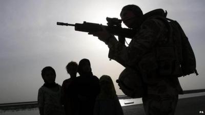 Children looking at a soldier holding up a gun in Basra, Iraq