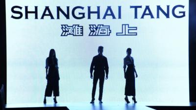 Models walk in front of Shanghai Tang logo