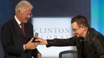 The lead singer of Irish rock group U2, Bono (R), bows as he hands the microphone to former U.S. President Bill Clinton after Bono had been imitating him on stage at the Clinton Global Initiative 2013