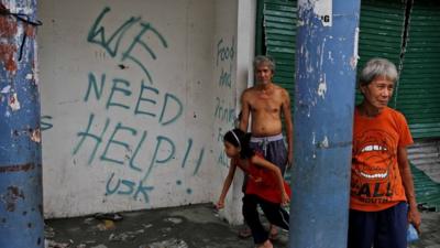 Residents in Tacloban stand next to grafitti requesting aid in the aftermath of Typhoon Haiyan