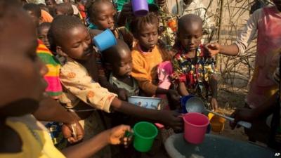 Children crowding round volunteer to collect rice porridge