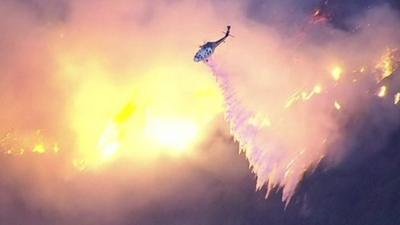 A helicopter douses flames in Southern California's San Gabriel Mountains