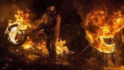 Activists of Euromaidan (the name given for Independence Square) burn tyres and warm themselves at a barricade in the center of Kiev early on January 24, 2014