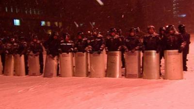 Riot police stand guard in the snow