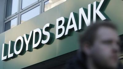 man walks past Lloyds Bank sign