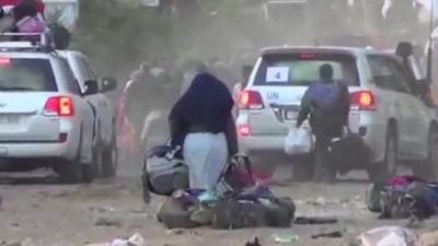 Woman carrying bags out of Homs