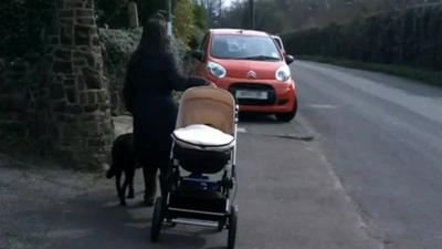 Blind woman with push chair and guide dog near car parked on pavement