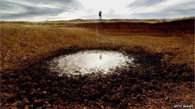 An Australian farmer inspects a dried up dam on his farm