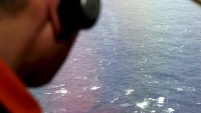 A crew member looks out of a window of a search plane