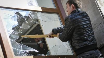 A pro-Russian protester breaks a window as they storm the regional government building in Donetsk April 6, 2014