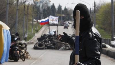 A pro-Russian militiaman gestures and holds a stick as he guards a barricade bearing the Russian flag