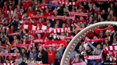 Fans holding football scarves and wheel showing names of the 96 dead