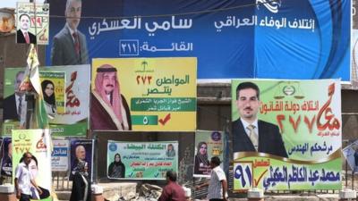 Iraqis walk past election posters in Baghdad (13 April 2014)