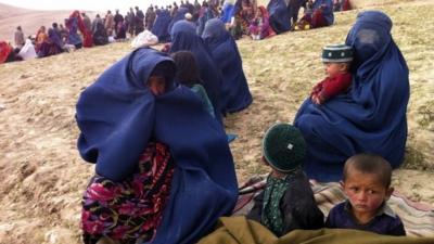 Survivors sit on a hillside as others watch the rescue effort near the site of Friday's landslide that buried Abi-Barik village in Badakhshan province