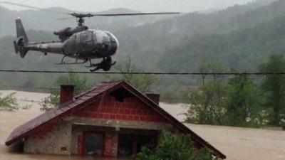 man hangs from underside of helicopter