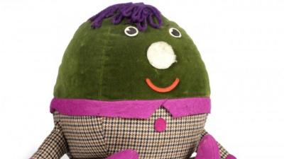 A Humpty Dumpty toy. It is a big, soft egg wearing a jacket with pink trim.