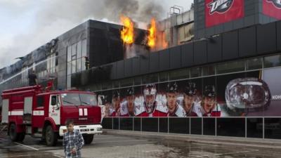 A boy walks by as firefighters attempt to extinguish a fire at the sports arena Druzhba , which is the home venue of the ice hockey club "Donbass", in Donetsk