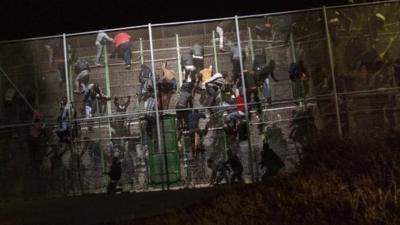 Sub-Saharan migrants scale a metallic fence that divides Morocco and the Spanish enclave of Melilla