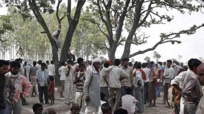 Onlookers stand at the site where two teenage girls, who were raped, were hanged from a tree