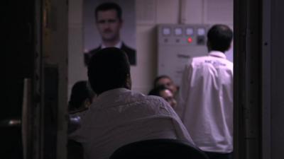 Men's backs with poster of President Assad in background