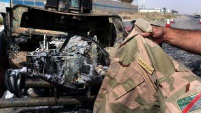 A man displays an Iraqi army jacket in front of a burnt out US-made Iraqi army HUMVEE vehicle at the Kukjali Iraqi Army checkpoint, some 10km of east of the northern city of Mosul, 11 June 2014