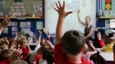 Children with their hands up in a school classroom