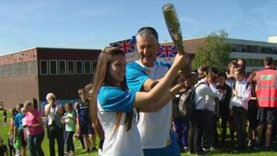 Student hands Queen's Baton to teacher Bob Foley at Newbattle High School