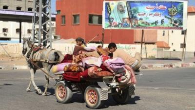 Palestinians ride a horse and cart in front of a billboard depicting late Hamas leaders, in the northern Gaza Strip, 14 July 2014