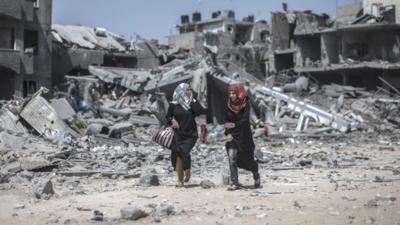 Two Palestinian women react to the scene of devastation behind them as they walk past destroyed houses in Beit Hanoun northern Gaza Strip, 26 July