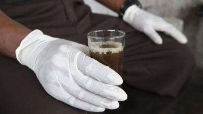 Liberian man holds a glass of Chinese tea with gloves to avoid contact with the deadly Ebola virus in Monrovia, Liberia, 31 July 2014