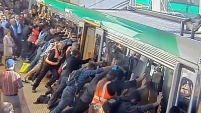 A frame grab from a video released on August 6, 2014 from the Public Transport Authority of Western Australia shows commuters pushing a train to free a passenger's leg trapped between the train and the gap in Perth. Dozens of Australians tilted a train to free a commuter whose leg was trapped between a carriage and a platform, with authorities praising their efforts as an example of "people power".