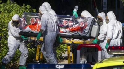 Health workers in protective gear wheel a stretcher into a hospital