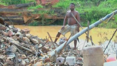 man standing on heap of rocks and rubbish next to stagnant pool