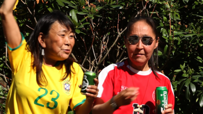 Two women in football T-shirts drinking beer. The woman on the left is cheering