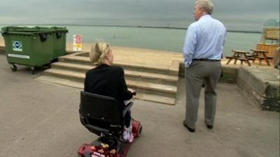 reporter in wheelchair looks at steps to beach