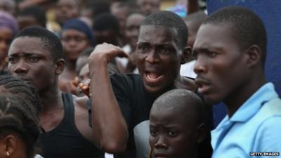 A crowd urges people in an Ebola isolation center to come out after a mob opened the gates the facility