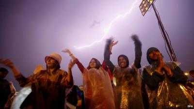 Protesters in waterproof covers, lightning strike above them