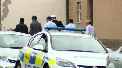 Pakistani men walk past a police car