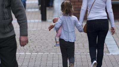 Anonymous small girl holding woman's hand and carrying a doll