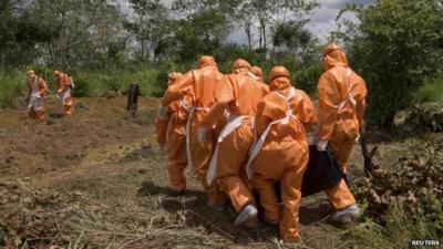 Burial team in protective clothing carrying Ebola victim in Port Loko, Sierra Leone