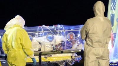 Medical workers in protective clothing with patient in covered stretcher