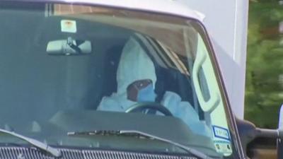 Healthcare worker, in full protective suit, drives the ambulance containing Amber Vinson