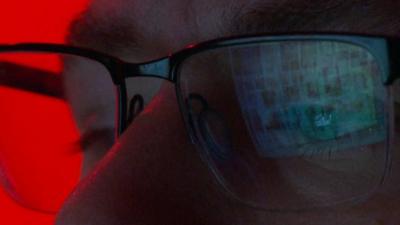 Close up of face of man in glasses with computer images reflected in lenses