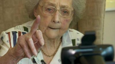 Dorothy Casford holds up finger at video device