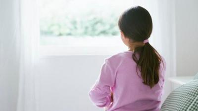 Young girl sitting alone on a bed.