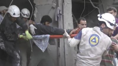 Men in hard hats pull an injued man from a building.