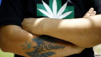 A man wearing a T-shirt with a marijuana leaf and a tattoo featuring a medicine symbol