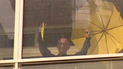 Chinese dissident Hu Jia waving yellow ribbon and umbrella from behind window of his apartment