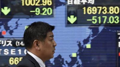 A pedestrian walks past a stock market board