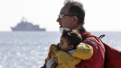 A rescuer carries a child evacuated from a cargo ship